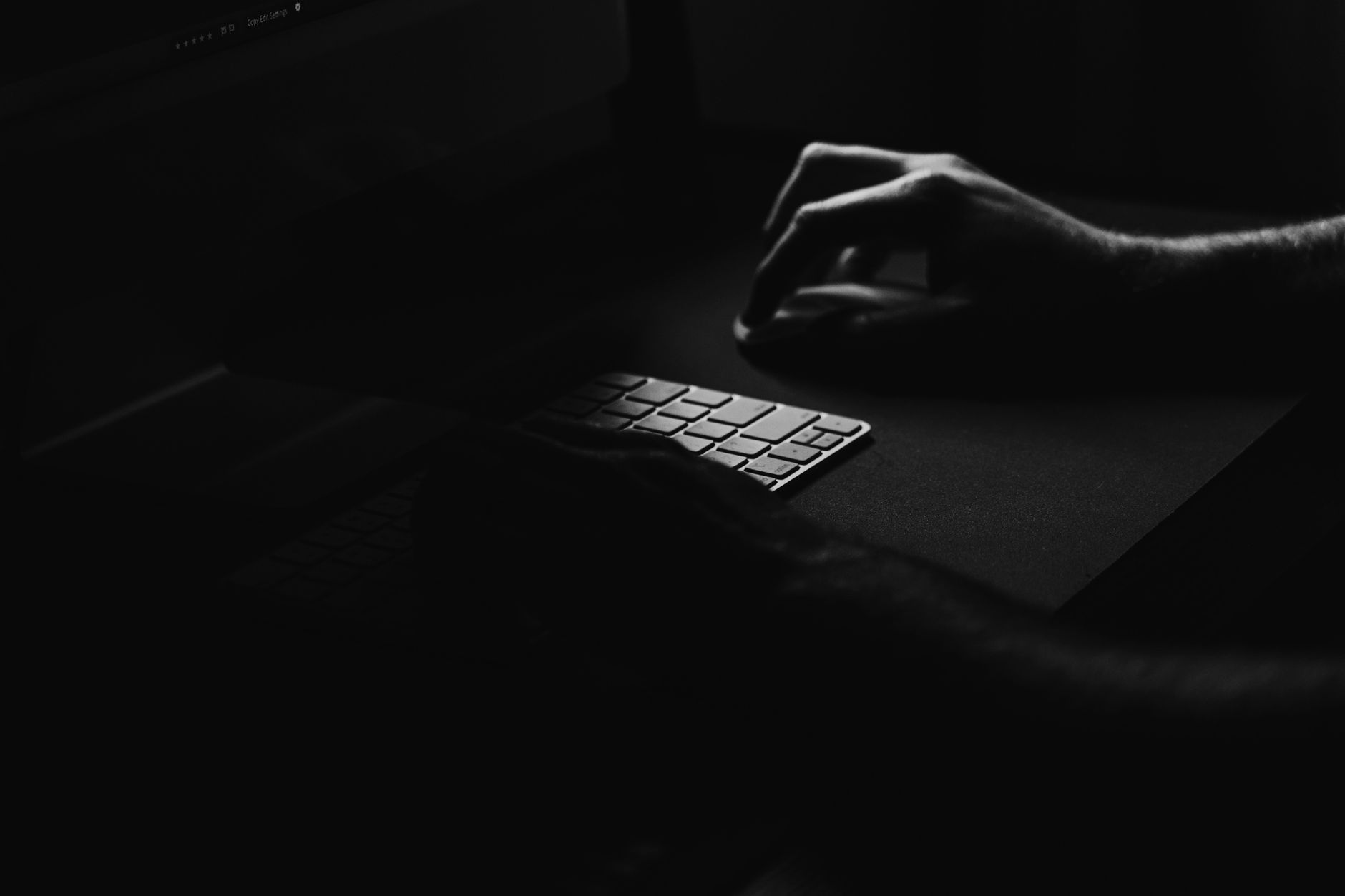 暗い部屋で、キーボードの上に手をかざしたまま止まっている手元のモノクロ写真。